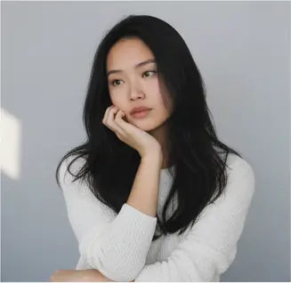 Half-body, ¾ front-facing, head slightly tilted right and resting on right hand, eyes looking to the left; left arm crossed under right elbow; shoulders relaxed, torso upright; eye-level camera angle, medium crop.