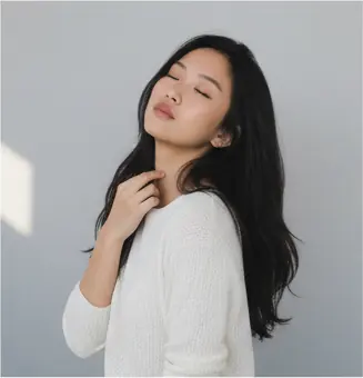 Half-body, ¾ side-facing, head tilted slightly back and to the left, eyes closed, relaxed expression; right hand touching neck, left arm out of frame; shoulders relaxed, torso straight; eye-level camera angle, medium crop.